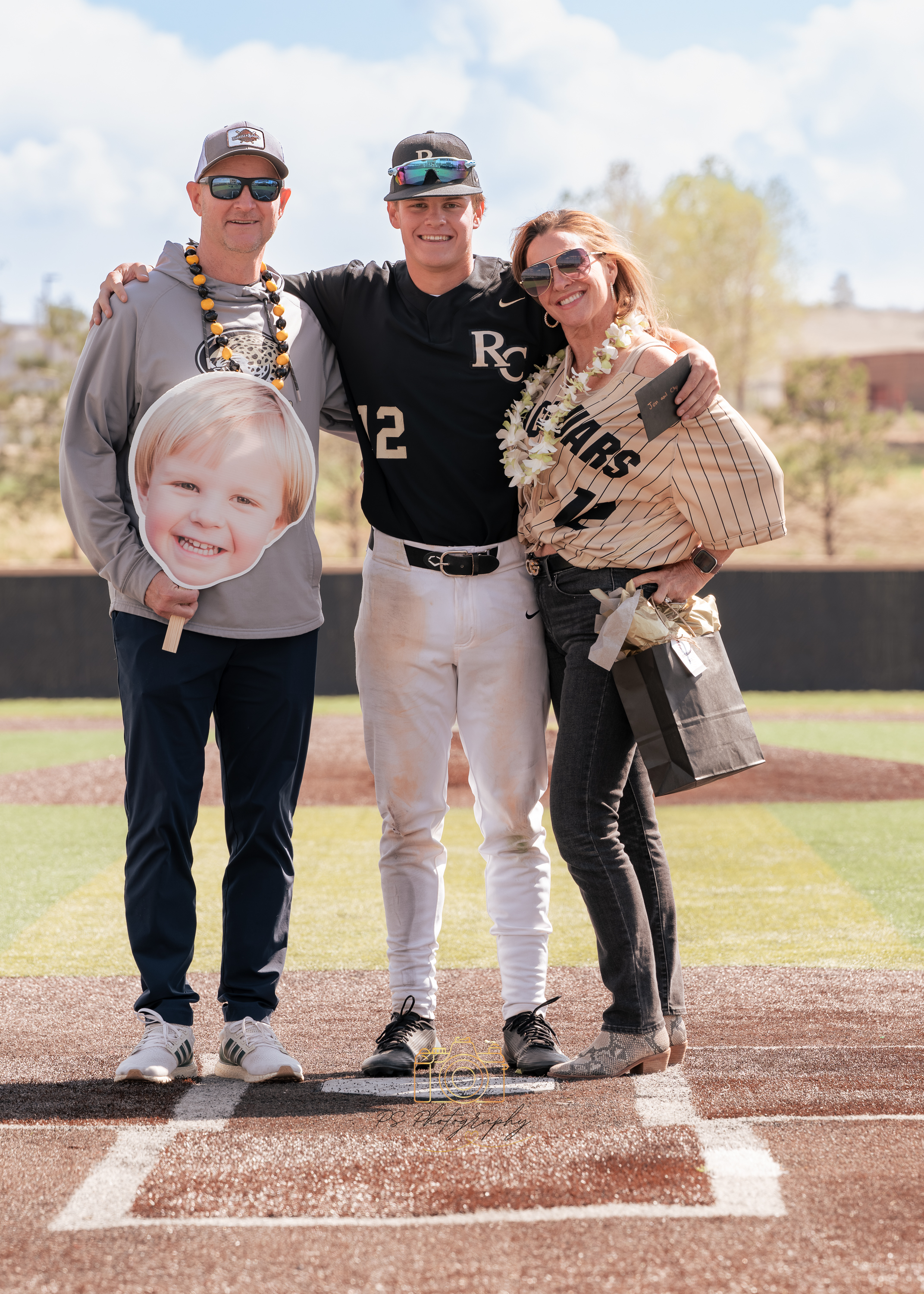 Senior baseball player standing with parents at home plate on senior night