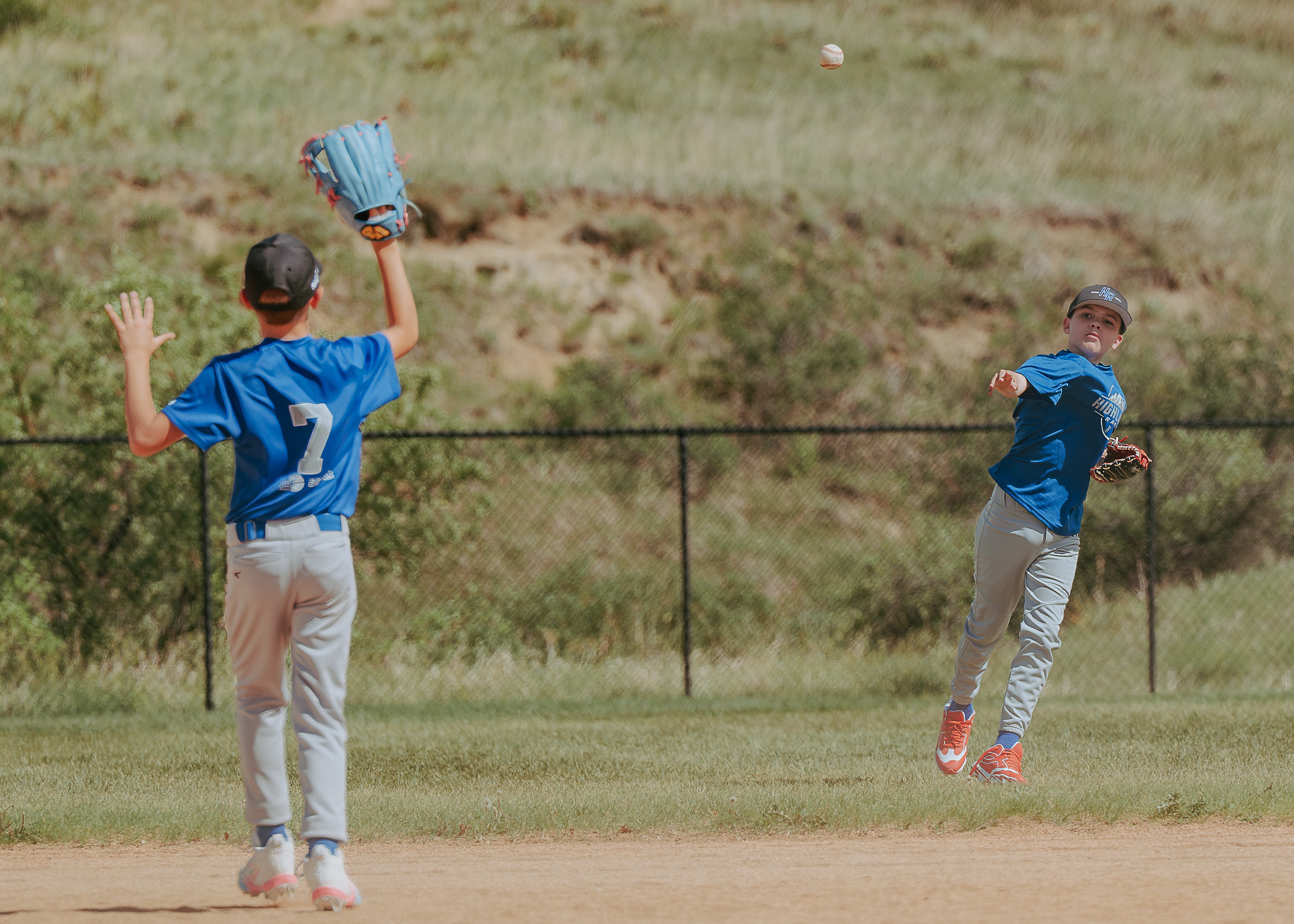 Youth baseball player making a throw across the infield while a teammate waits with glove raised
