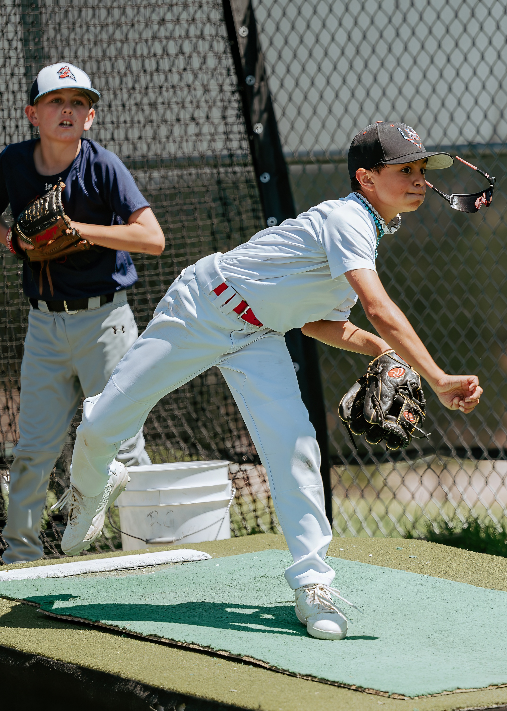 Youth baseball pitcher working from a bullpen mound while another player watches nearby