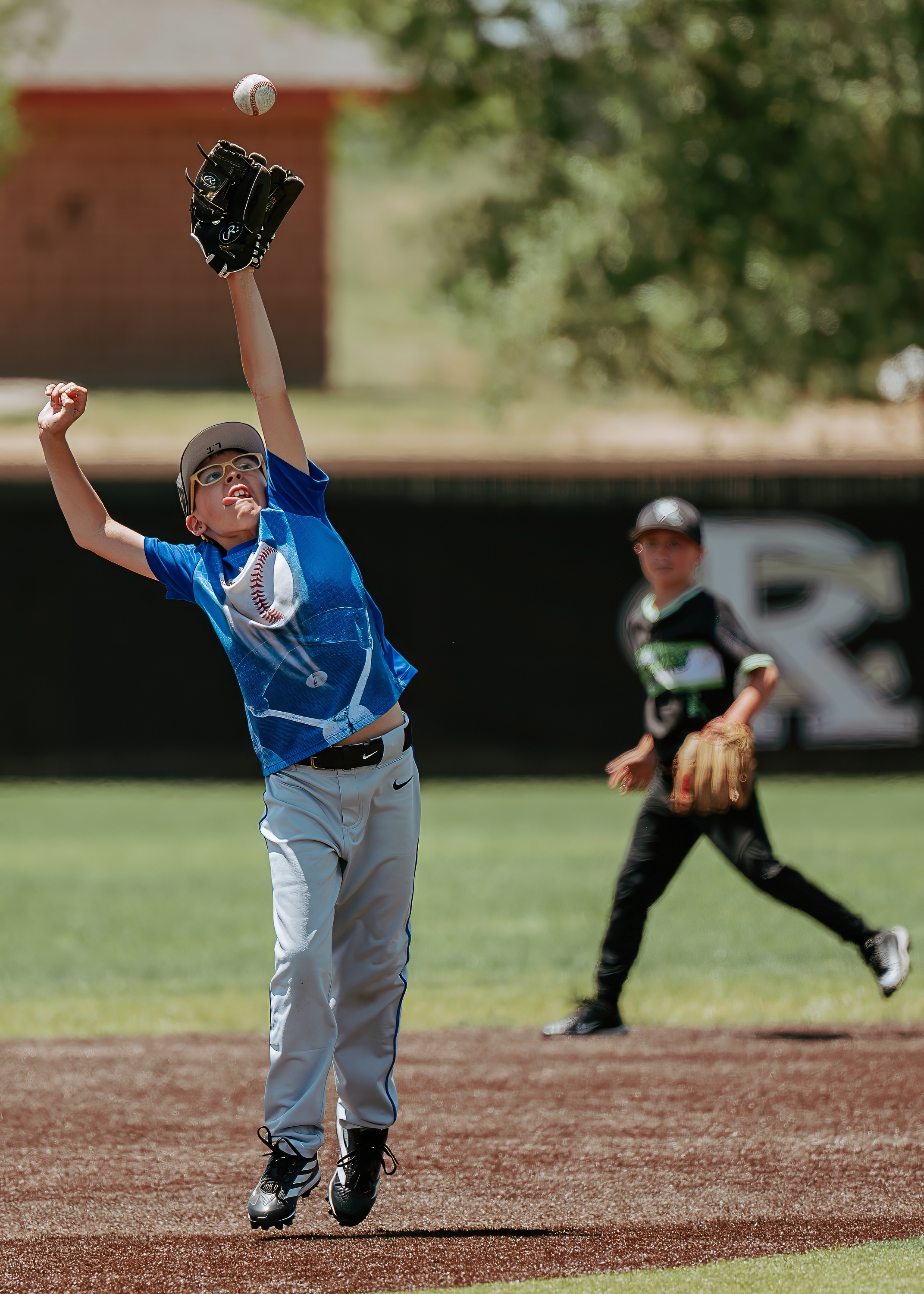 Youth baseball player reaching high into the air for a full extension catch