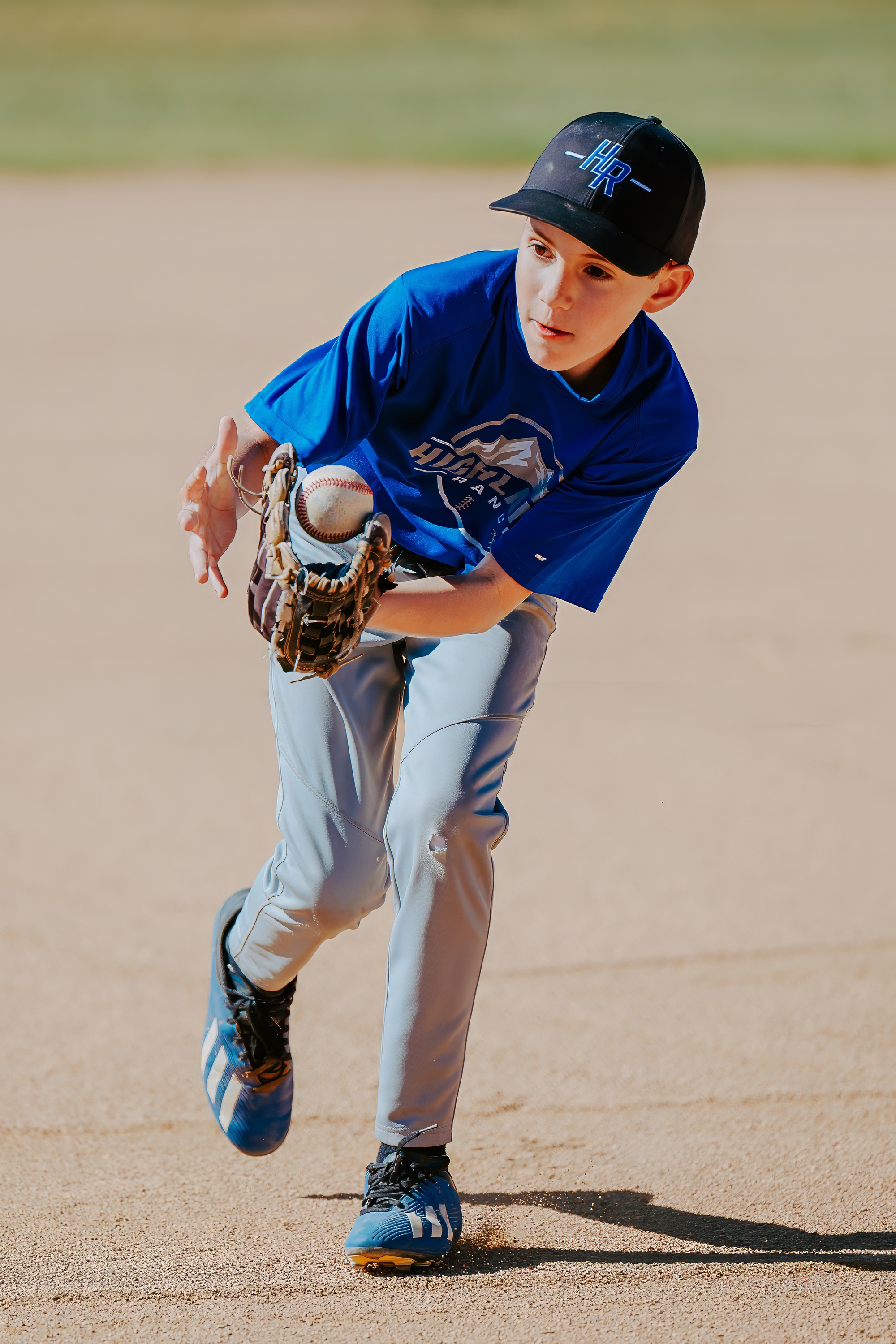Youth baseball player fielding the ball while running across the dirt infield