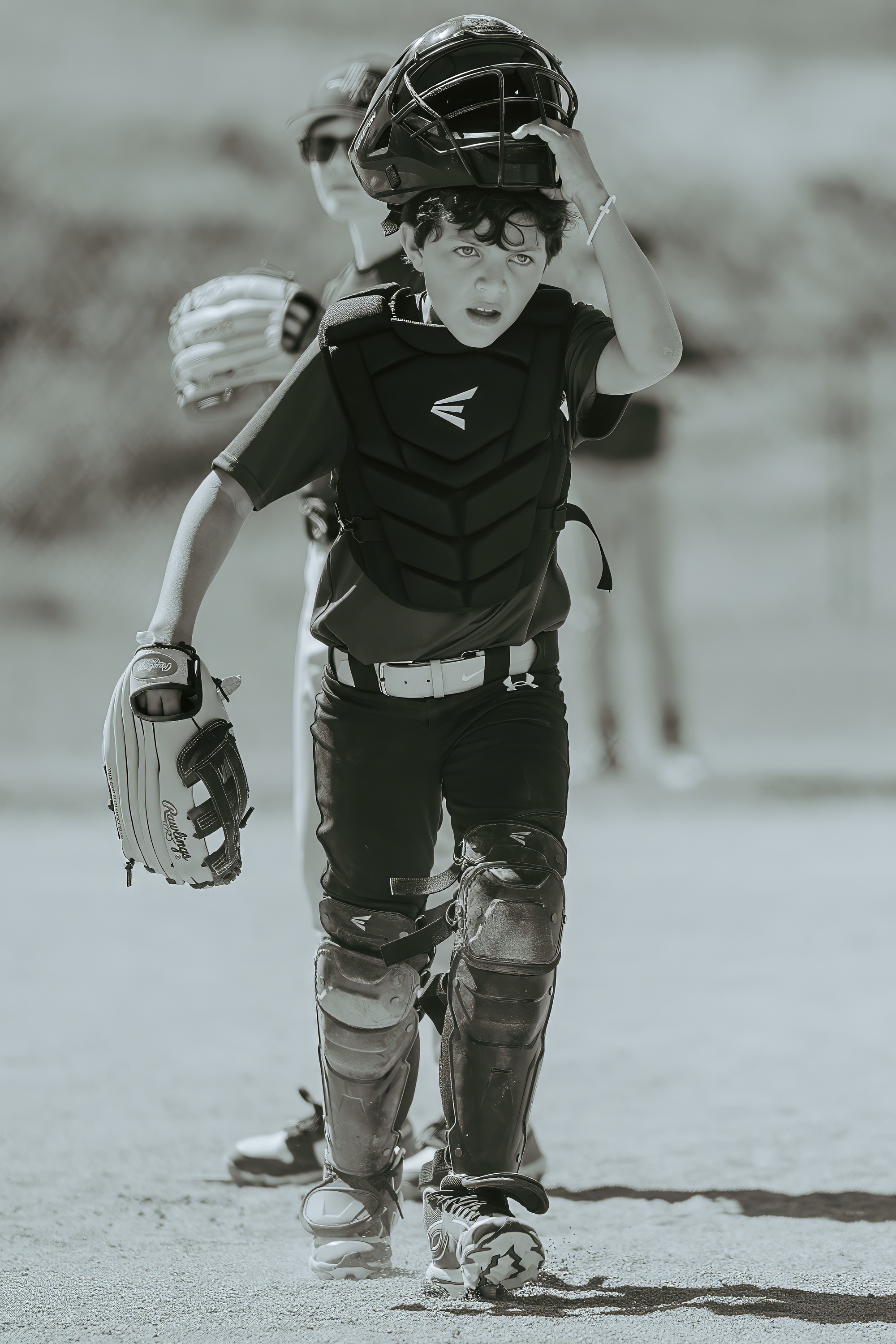 Youth baseball catcher walking off the field with helmet lifted after a play