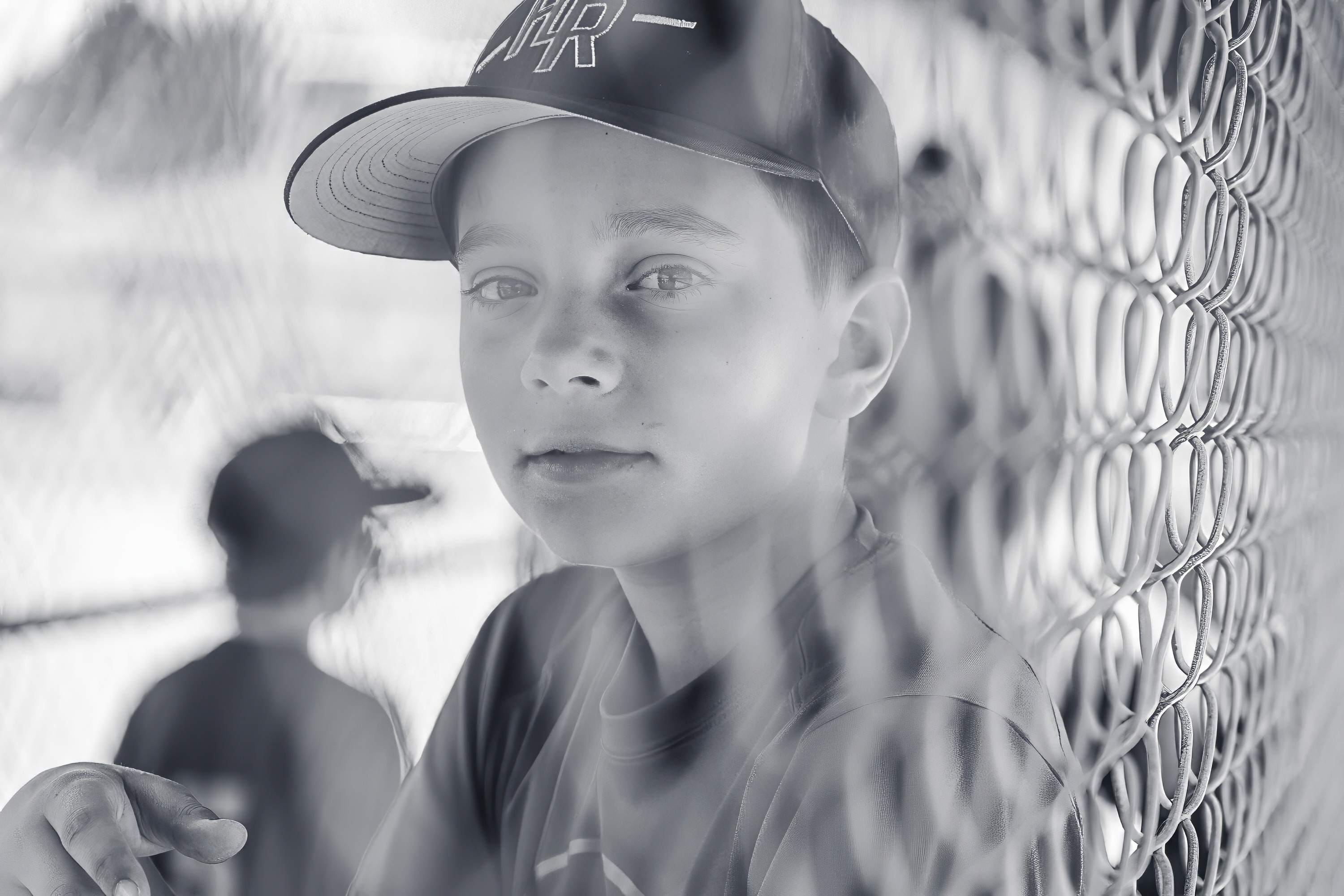 Black and white portrait of a youth baseball player looking through a dugout fence
